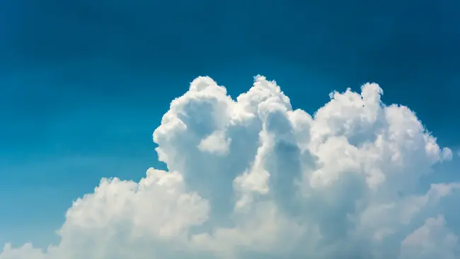 A large white cumulus cloud building against a clear blue sky