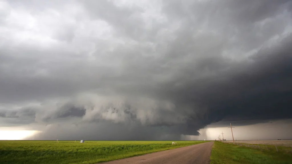 Dark shelf cloud from a severe thunderstorm rolling over farmland, with a straight road and power lines leading toward the horizon