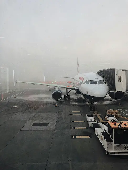 A passenger plane at an airport gate, ground crew and boarding bridge nearby, visibility reduced by thick fog