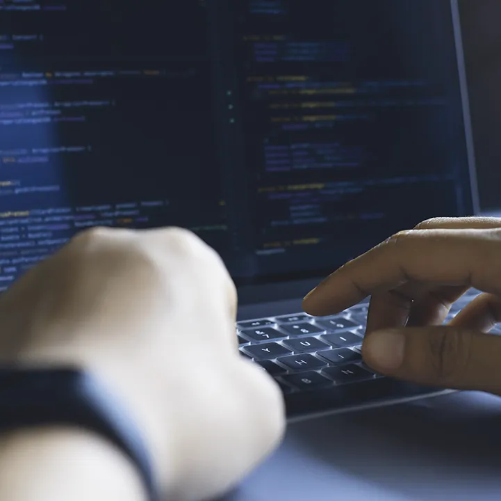 Entwickler tippt auf einem Laptop, Codezeilen auf dem Bildschirm