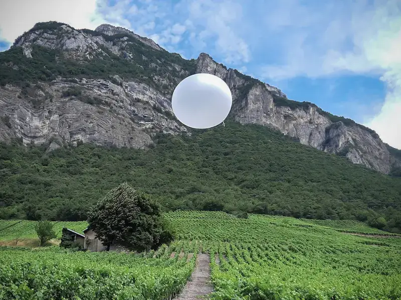Ballon d'ensemencement des nuages LAICO de SELERYS survolant un vignoble au pied d'une montagne